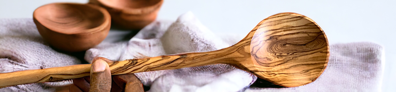 Kitchen Essentials category image showing a long olive wood stirring spoon and two small bowls displayed atop towels on a kitchen counter.