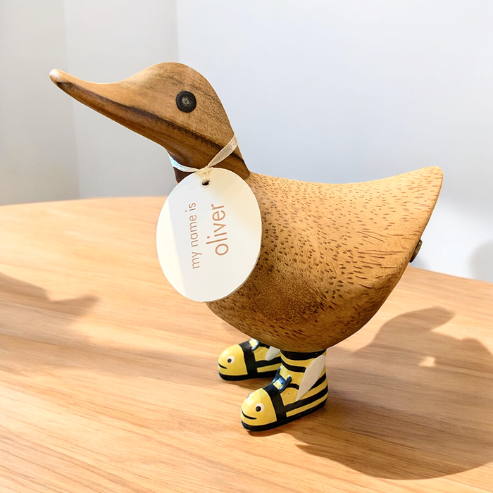 Cute wooden duck with name tag wearing bumblebee boots on a wooden table