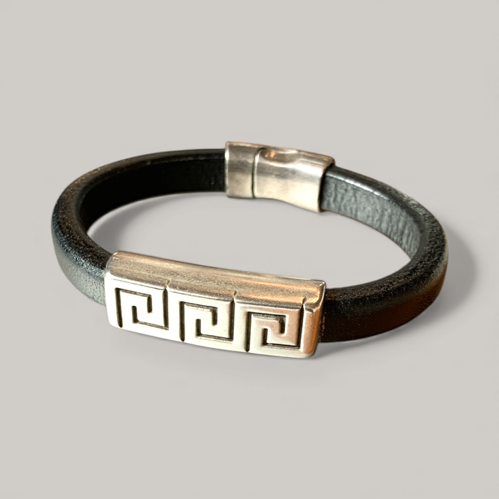 Black leather bracelet with metallic clasp and decorative element on a gray background