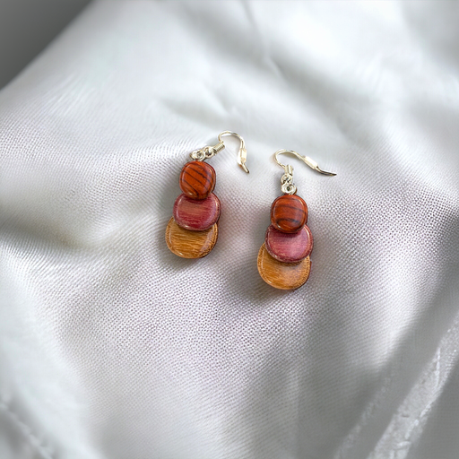 Stylish small wood earrings with overlapping discs in purple heart, cocobola, and pau amarillo, displayed on white fabric
