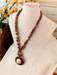 Handmade Necklace Elizabeth in assorted exotic woods, featuring a round pendant, displayed on a bust with flowers in the background.