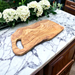Extra large olive wood cutting board great for entertaining. Exceptionally beautiful wood  grain.  Looks more like burl wood. Displayed on white marble countertop alongside white hydrangeas.