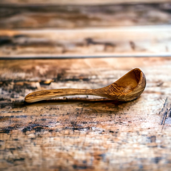 Large olive wood ladle with beautiful grain on rustic wood surface. Buy at Barouke.