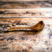 Large olive wood ladle with beautiful grain on rustic wood surface. Buy at Barouke.